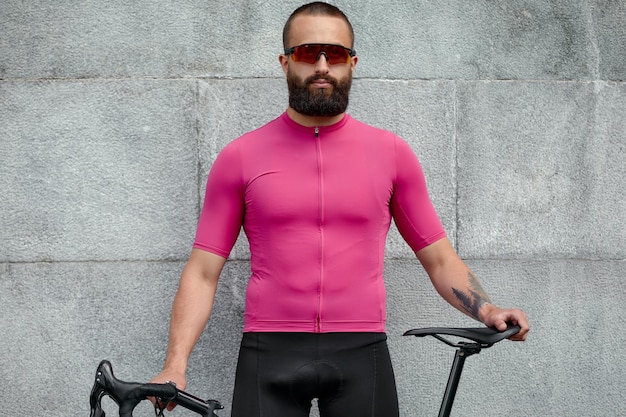 Cyclist in pink sportwear resting after an workout while standing against cement wall background with copy space area for text message or advertising