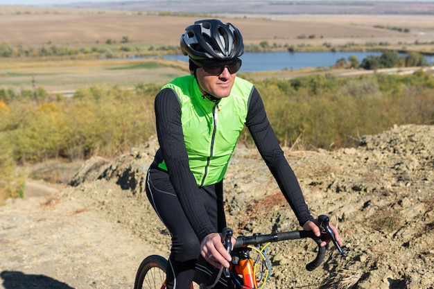 Cyclist riding bicycle on offroad against clear sky A man in an outfit stands with a bicycle on an autumn sunny day