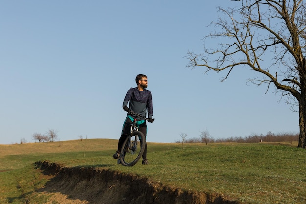 Cyclist in shorts and jersey on a carbon hardtail bike with an suspension fork standing on a cliff