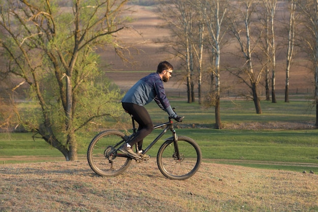 Cyclist in shorts and jersey on a modern carbon hardtail bike with an air suspension fork standing on a cliff against the background of fresh green spring forest