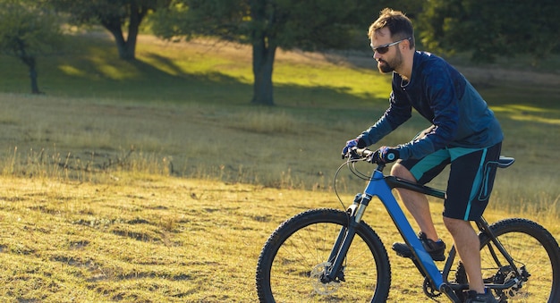 Cyclist in shorts and jersey on a modern carbon hardtail bike with an air suspension fork standing on a cliff against the background of fresh green spring forest