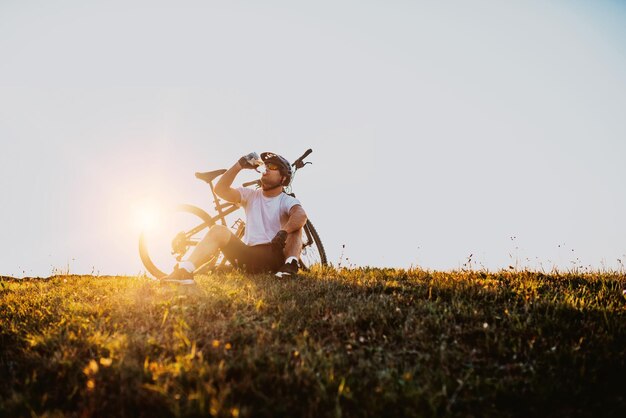 The cyclist sits in a meadow while resting from a strenuous ride on mountain roads. The cyclist is cooled by water. Selective focus. High-quality photo