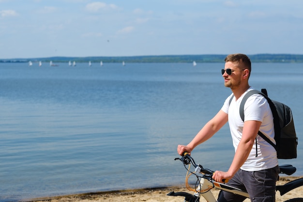 A cyclist with a backpack and glasses rides along the sea on a bicycle on a beautiful sunny day.