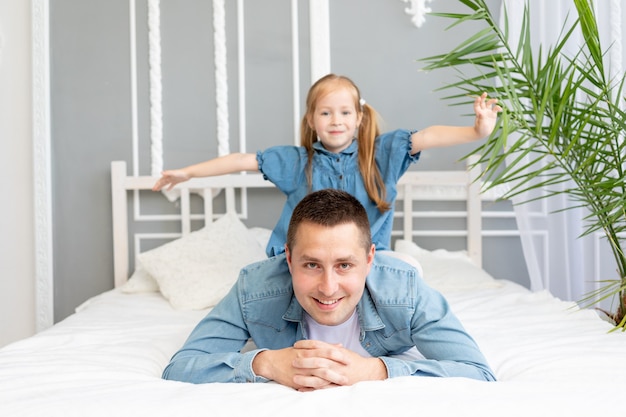 Dad and baby daughter have fun playing and cuddling at home on the bed