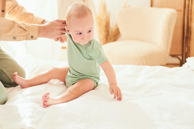 Dad changes the clothes of his young son sitting on the bed