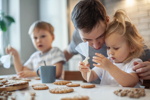 Dad and children decorate christmas gingerbread at home a boy and a girl paint with cornets with sug...