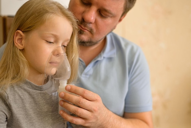 dad helps his sick child do inhalation with a nebulizer at home he holds a mask from which steam