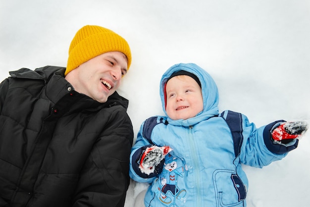 Dad and his son lie in the snow and look up A little boy and his father playing in winter Outdoor recreation of a family with children in winter A child on a walk in a snowcovered winter park