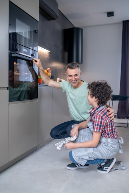 Dad hugging son crouched near working oven