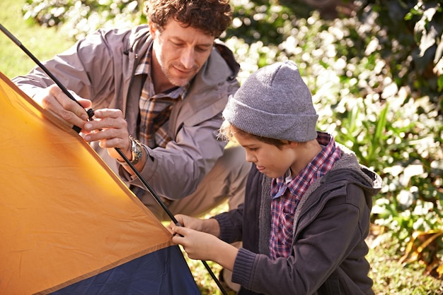 Dad kid and set up tent for camping outdoor in nature on vacation while bonding in summer Father boy and preparing campsite learning and helping in forest for travel education and holiday