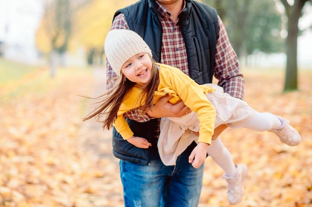 Dad in a plaid shirt tosses his five-year-old daughter in his arms in an autumn park