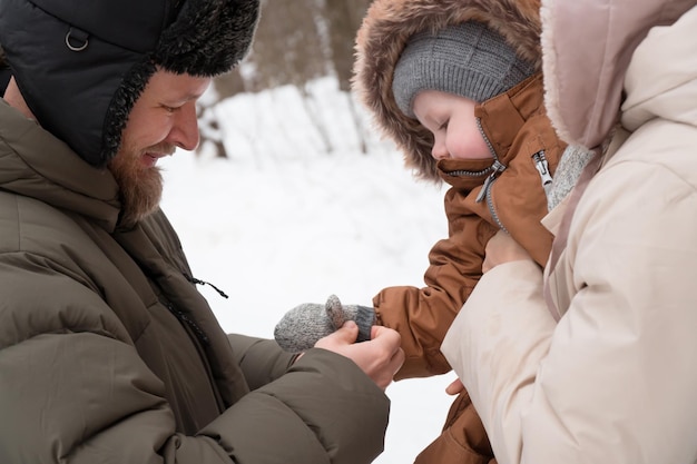 dad puts mitten on baby son hand walking outdoor in winter