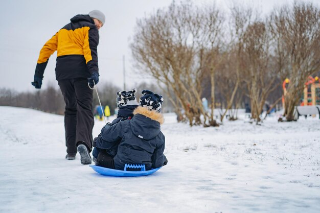 Dad ride his kids on sled in park. Winter activities. Happy family weekend on snowy day. Image with selective focus . High quality photo