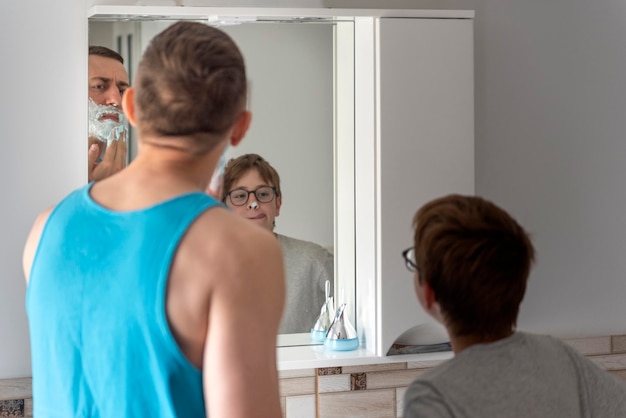 Dad and son in bathroom in front of mirror together Young father and his teenage son with shaving foam on his nose