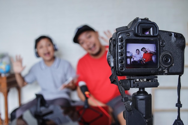 Dad and son greeting online followers while doing video streaming. Asian family spending quality tim