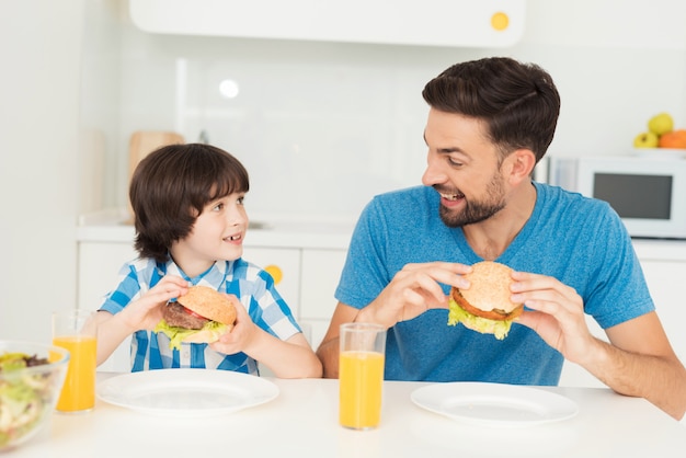 Dad and son look at each other while eating.