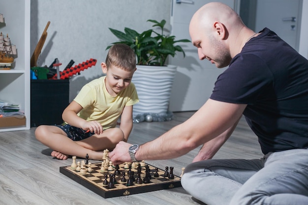 Dad and son play chess on the floor in the children's room among the toys