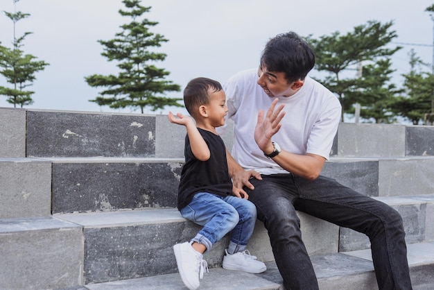 Dad and son playing. Father asking son to high five while sitting together at the park.