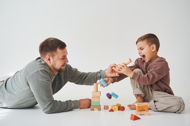 Dad and son smiling having fun and playing colored bricks toy on white background Paternity Caring father with his child