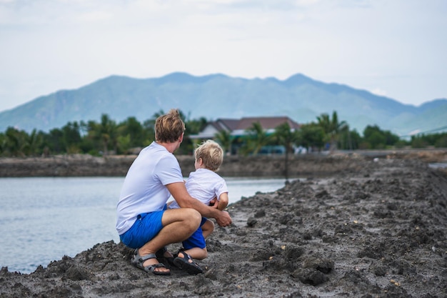 Dad squatting hugging son holding hands together near lake looking far away Happy childhood fatherhood Family together walk play Home natural education fathers day responsibilities influence