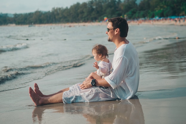 Dad in sunglasses holds the baby in his arms on the beach. The concept of educating the father of young children, Happy childhood, a friendly family.