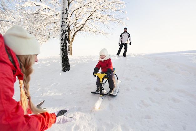 Dad takes his son down the mountain in the white snow on a sled in winter while mom catches