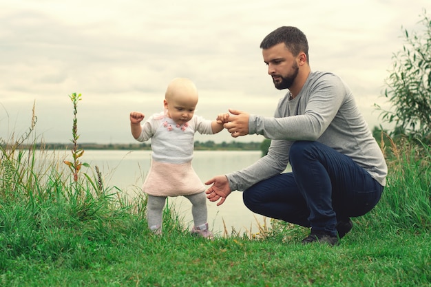 Dad teaches daughter to walk, park, nature. Walk on the grass. Father and daughter. First steps.