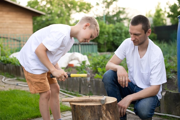 Dad teaches his son to hammer nails into a tree