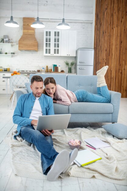 Dad with a laptop sitting on the floor on a plaid and daughter lying on the sofa in thick socks