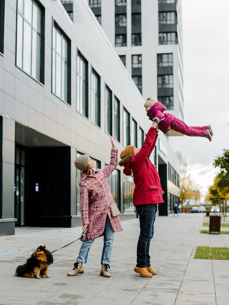 Daddy tossing his infant son up on background of apartment houses in city outdoors