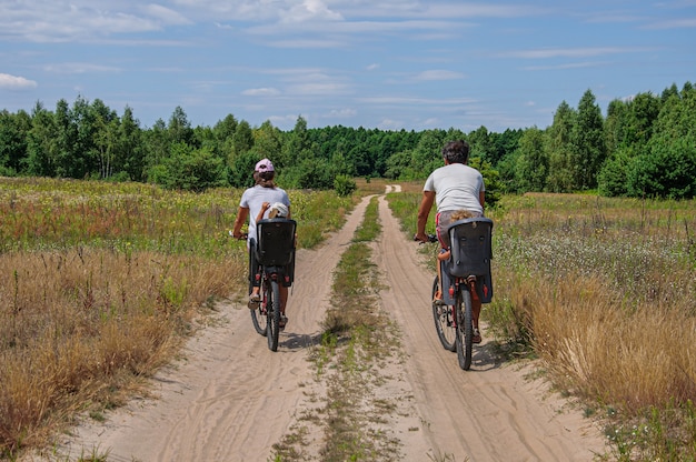 Dads ride their children in bicycle seats on a dirt road through the forest