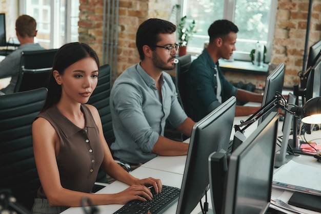 Daily routine group of young employees working on computers while sitting in modern open space