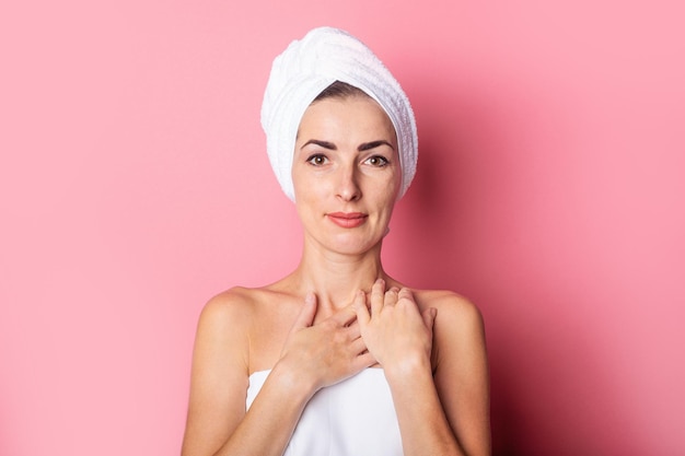 Daily spa Young woman with a towel on her head head touching her soft skin on the neck on a pink background