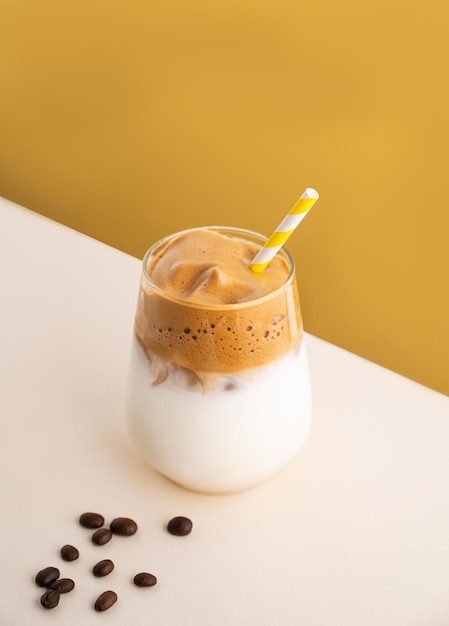 Dalgona coffee with milk in a glass with ice cubes and grains on a yellow background The concept of a cold summer drink Top view and copy space