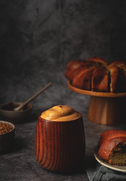 Dalgona coffee in a wooden cup and a cake on a stand. Fluffy whipped coffee. Trend korean drink.