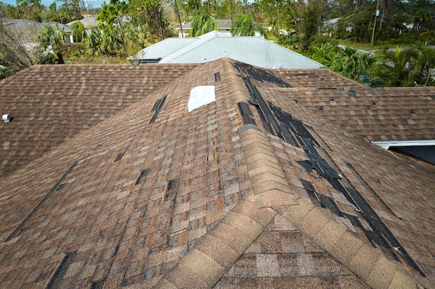 Damaged house roof with missing shingles after hurricane Ian in Florida Consequences of natural disaster