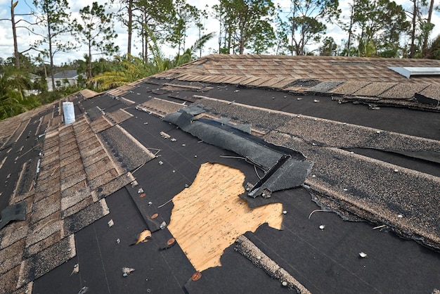 Damaged house roof with missing shingles after hurricane Ian in Florida Consequences of natural disaster