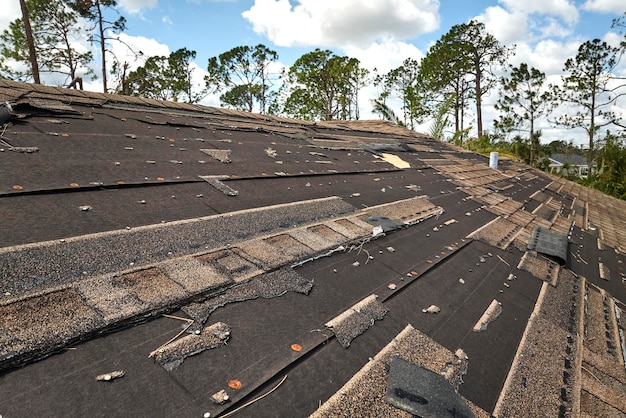 Damaged house roof with missing shingles after hurricane Ian in Florida Consequences of natural disaster