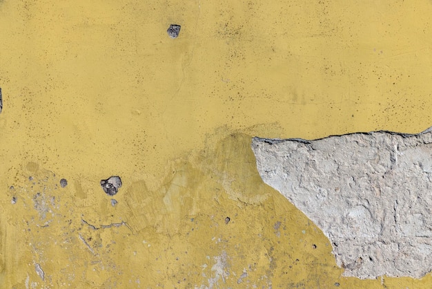 Damaged yellow plaster of a concrete wall