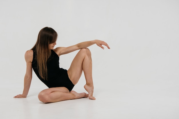 Dancer with long blond hair in a black dance leotard sits in the studio on a white background.