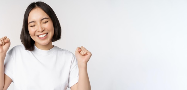 Dancing asian girl celebrating feeling happy and upbeat smiling broadly standing over studio white background