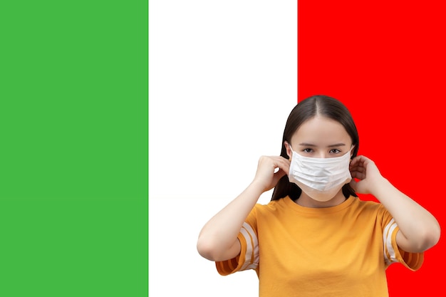 The danger of coronavirus in Italy Young girl in antibacterial medical mask on a flag background with copyspace