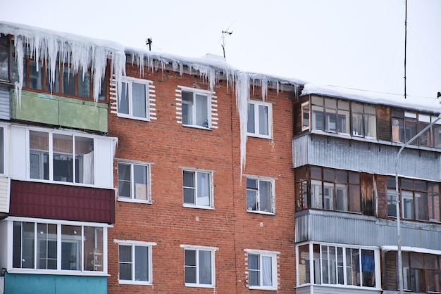 Dangerous giant icicles hanging down from the roof of residential brick house Harsh nord winter