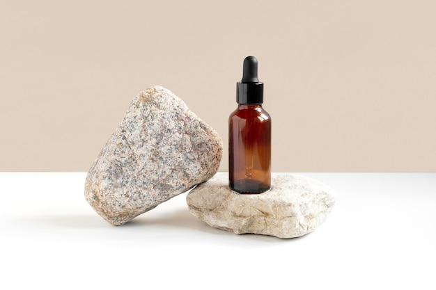 Dark amber glass bottle standing on stone Natural skin care SPA beauty product design Mineral organic oil cosmetics on beige background MockUp Oily pipette Face and body treatment Front view