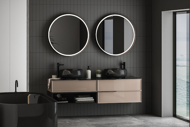 Dark bathroom interior with concrete floor, black bathtub and oval mirrors, double sink, side view.