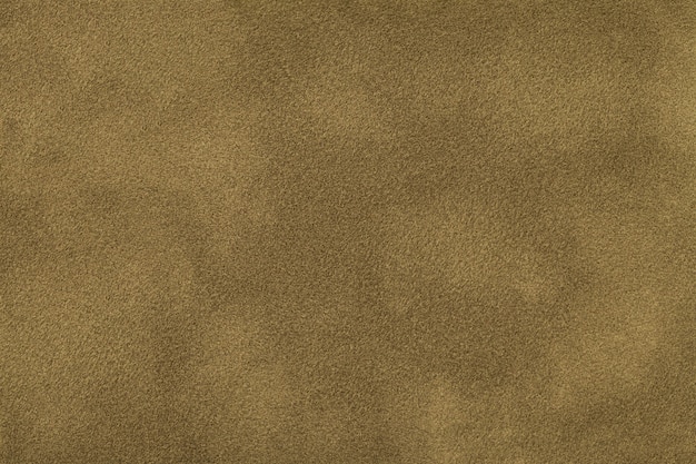 Dark beige matte background of suede fabric, closeup. Velvet texture of seamless brown felt textile, macro.