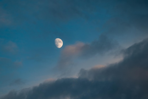 Photo dark blue sky with clouds and young white moon on it