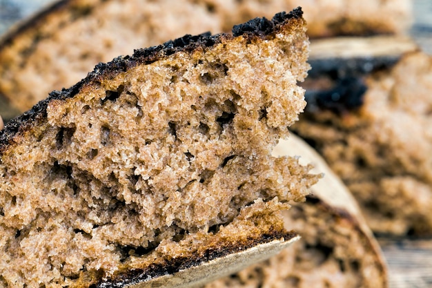 Dark bread with a crisp crust on a wooden table, bread broken into a large number of pieces, soft and delicious flesh