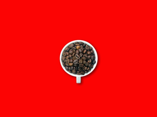 Dark brown coffee beans in white coffee cup and saucer in ther center picture. Red background.