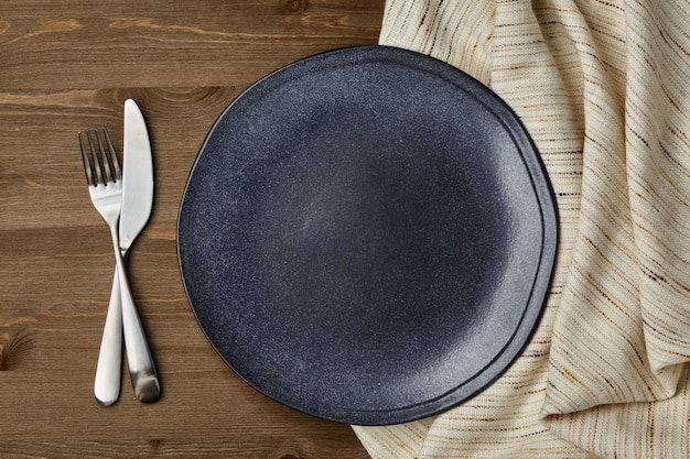 Dark ceramic plate and crumpled linen tablecloth and cutlery on a wooden table